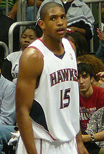 A basketball player, wearing a white jersey with the word «ATLANTA» and the number 15 on the front, stands on a basketball court.