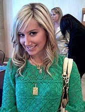 Юная блондинка улыбается, на ней надета зелёная блузка и три золотых цепи на шее, на одной из которых висит золотая медаль