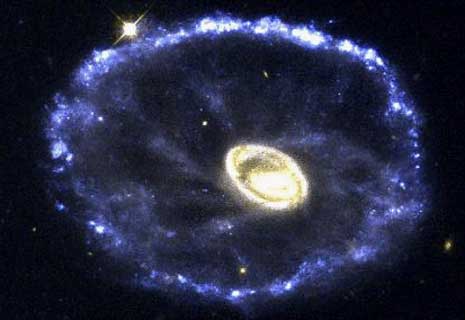 ЛОБОВОЕ СТОЛКНОВЕНИЕ В КОСМОСЕ ПРИВОДИТ К РОЖДЕНИЮ ЗВЕЗД. Редкое и захватывающее лобовое столкновение двух галактик запечатлел на цветном снимке (справа) космический телескоп им. Хаббла. Объект, расположенный на расстоянии 500 млн. световых лет в направлении созвездия Скульптор, называют Тележное Колесо. Яркое кольцо возникло в результате пролета маленькой галактики - одной из двух, находящихся справа. Столкновение привело к гигантскому выделению энергии и заставило газ и пыль раздвигаться со скоростью 320 тыс. км/час. Эта расширяющаяся волна стимулировала рождение звезд. В кольце содержится несколько миллиардов новорожденных звезд. На снимке (слева вверху) в кольце видны уплотнения, представляющие крупные скопления молодых звезд. На изображении центра галактики (слева внизу) видно огромное количество пыли и областей звездообразования. Яркие точки - это огромные звездные скопления.