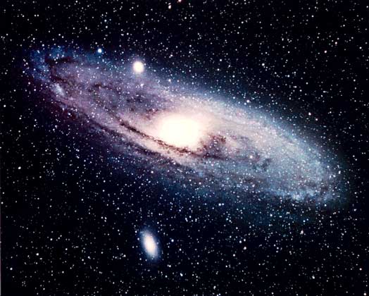 Рис. 3. ЗВЕЗДНЫЕ НАСЕЛЕНИЯ. На фотографии спиральной галактики Туманности Андромеды видно, что в ее диске сосредоточены голубые гиганты и сверхгиганты Населения I, а центральная часть состоит из красных звезд Населения II. Видны также спутники Туманности Андромеды: галактика NGC 205 (внизу) и М 32 (вверху слева). Самые яркие звезды на этом фото принадлежат нашей Галактике.
