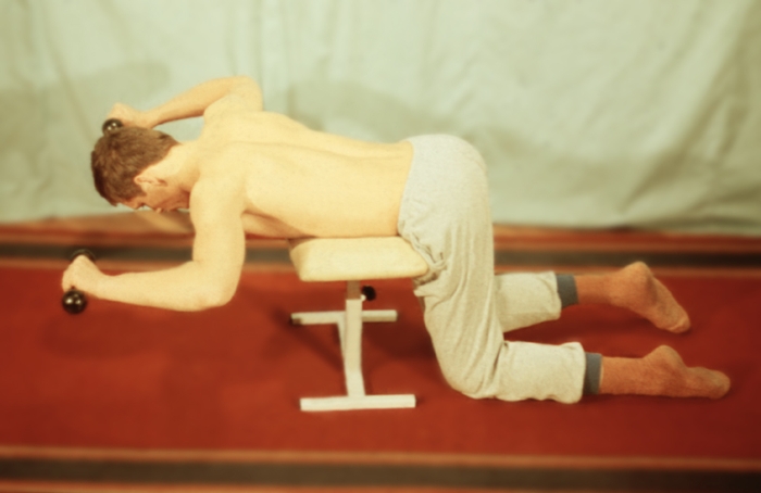 Рис. 12е). Физические упражнения для восстановления функции плечевого сустава с дополнительным отягощением и эспандером: упражнение с гантелями стоя на коленях и опираясь грудью на табурет