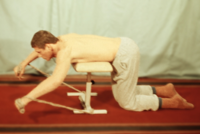Рис. 12з). Физические упражнения для восстановления функции плечевого сустава с дополнительным отягощением и эспандером: упражнение с эспандером стоя на коленях и опираясь грудью на табурет