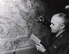 A balding man holding a small card titled «Ship’s Position» writes a black line on a map of the Earth.