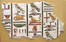 Каменный фрагмент с ярко окрашенными цветами и рельефные изображения египетских иероглифов, написанных в вертикальных колонках, на бежевом фоне