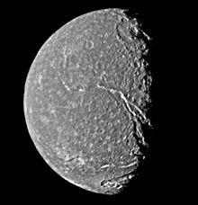 Круглое сферическое тело, освещенной с левой стороны. На внешней темной поверхности отчетливо видны яркие пестрые пятна.