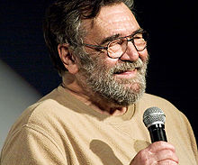 Бородатый мужчина в очках, держащий микрофон